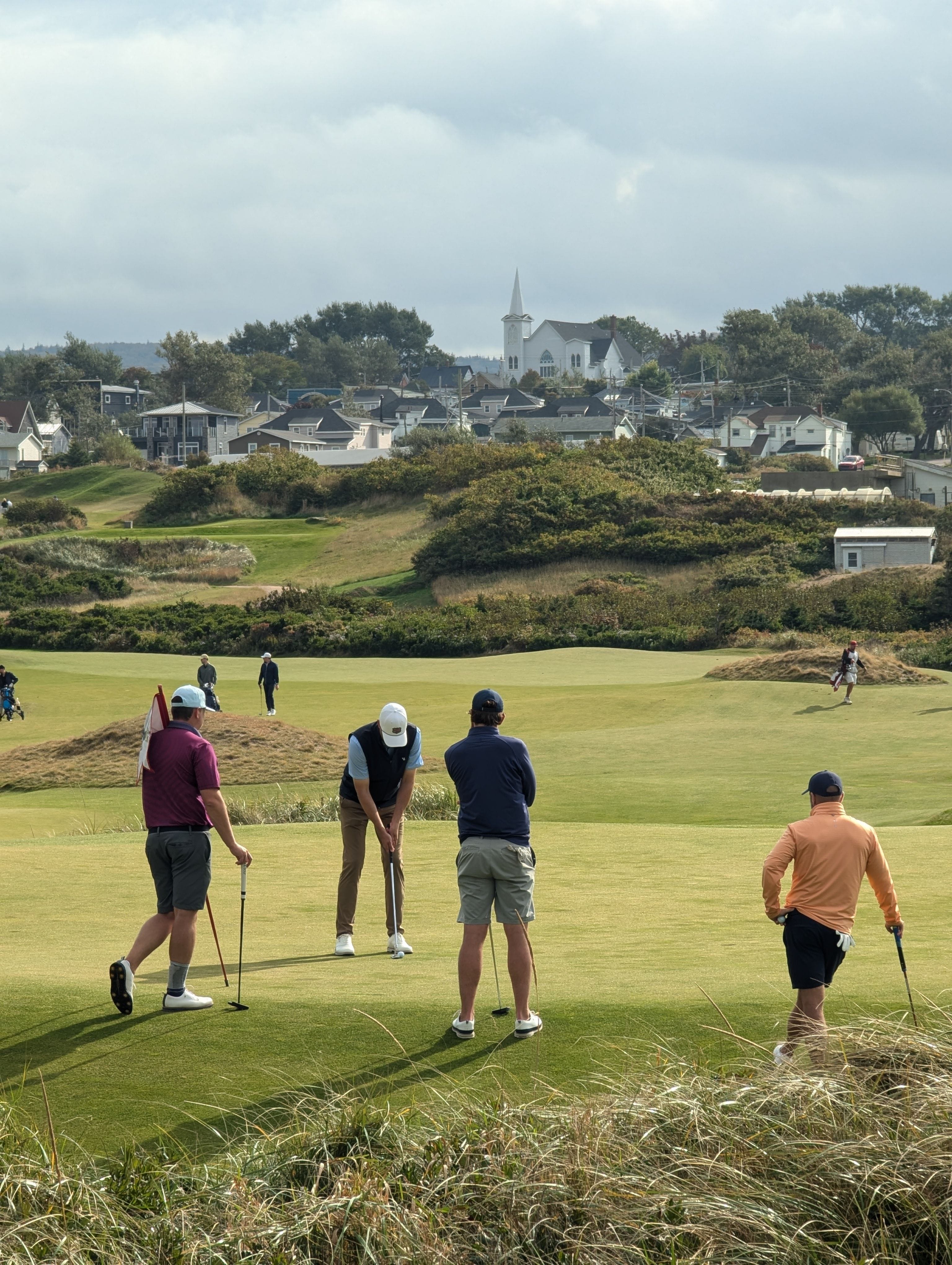 Four golfers on a links-style green with a coastal town in the distance
