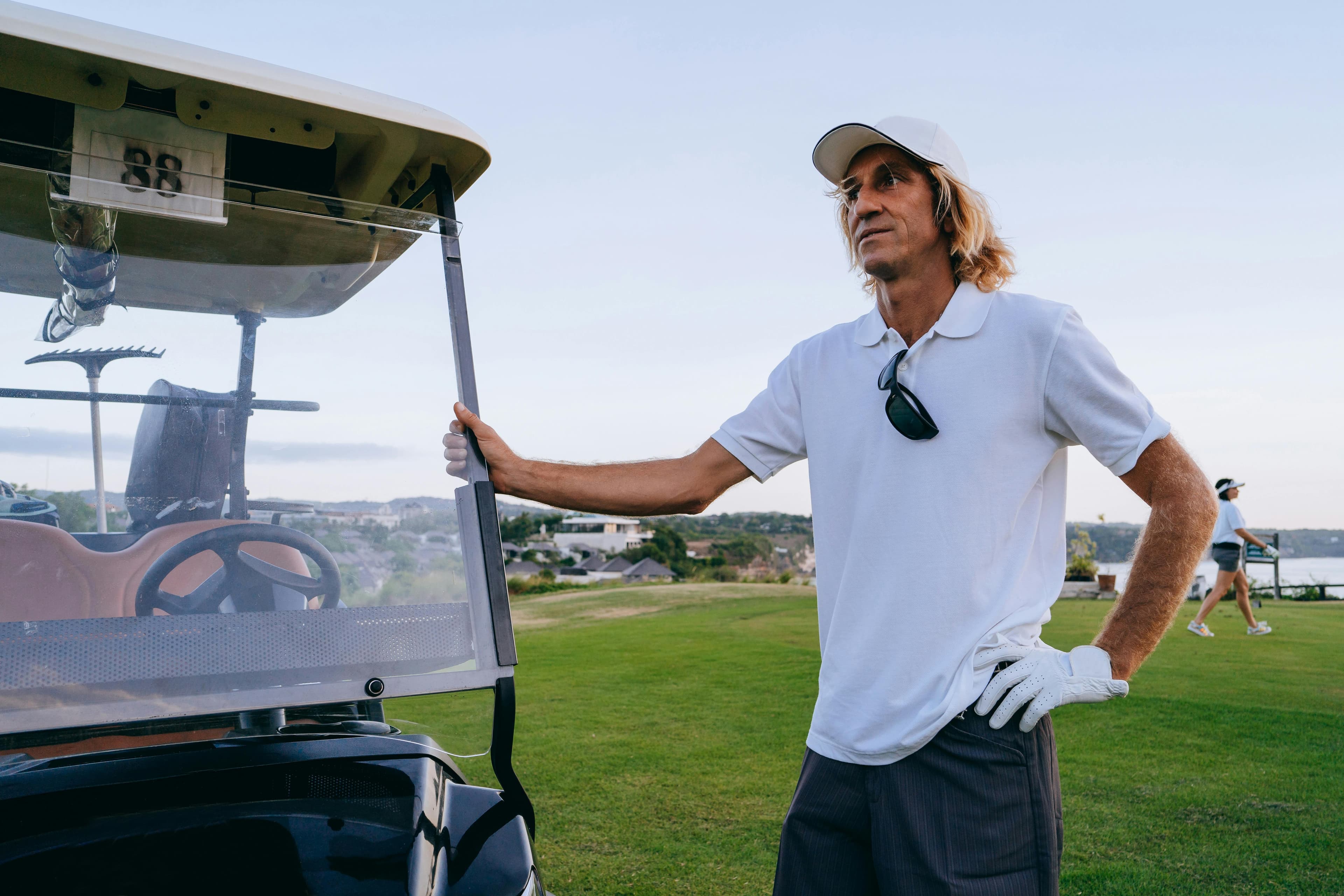 Man in white shirt by a golf cart on a lush golf course