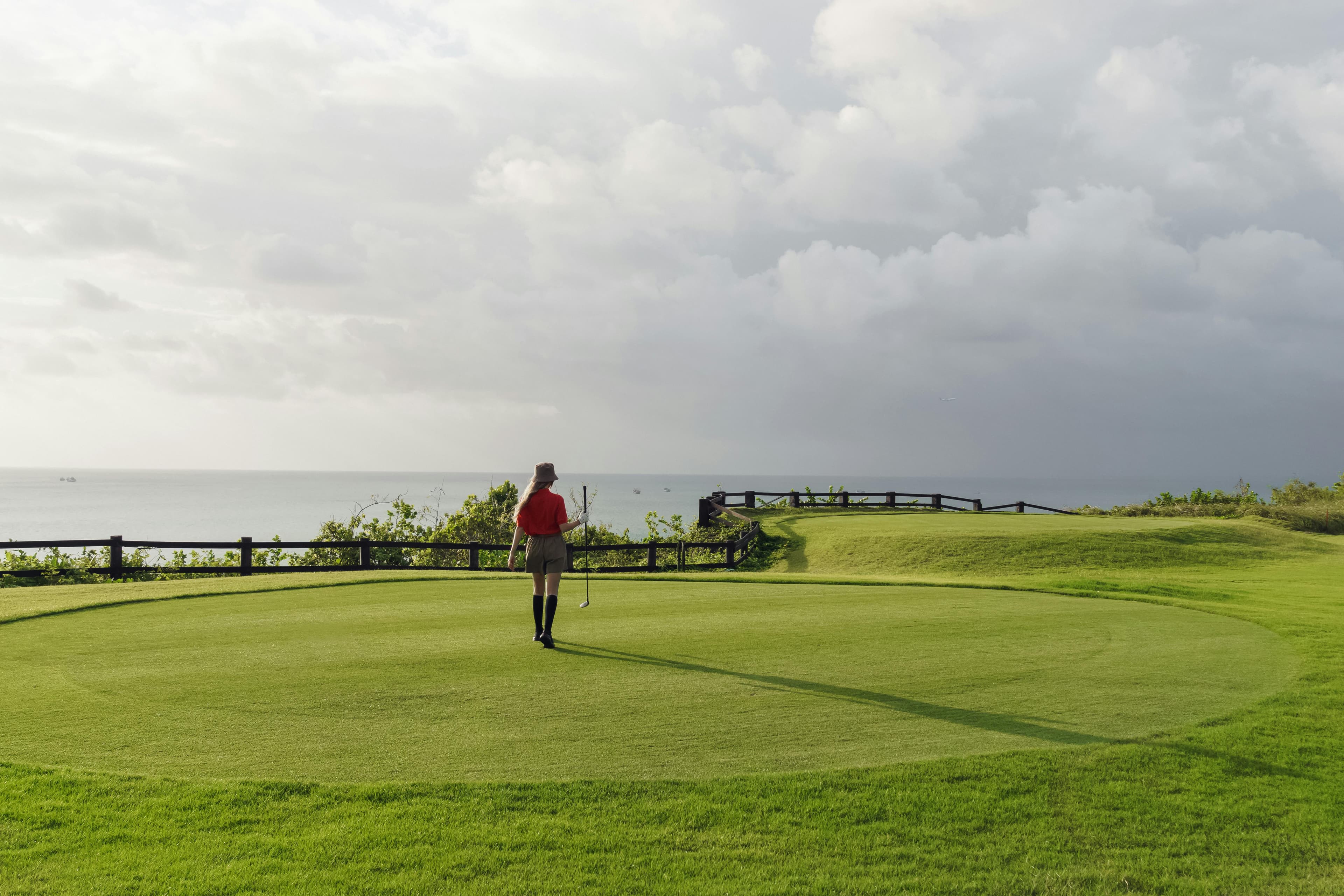Woman playing golf on a scenic coastal course under a partly cloudy sky